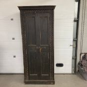 An Indian carved hall or pantry cupboard with panel doors enclosing a distressed painted interior