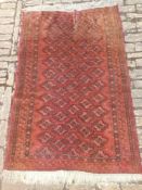A Turkoman carpet with repeating motifs on a burgundy ground within stylised geometric borders.