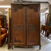 A 19th century French provincial oak armoire having a heavily carved crest and frieze over a pair of