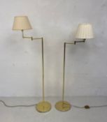 A near pair of brass floor standing lamps each with a single articulated arm raised on a narrow stem