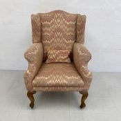 An early 20th century wingback armchair having a serpentine back with shaped and scrolled arms