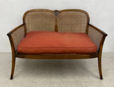 An early 20th century walnut two seater bergere sofa with caned back and sides on outswept