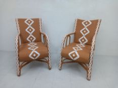 A pair of vintage style wicker armchairs each having a slanted back with curved arms over a deep