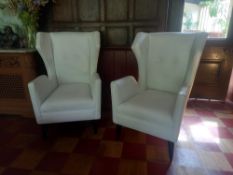 A pair of contemporary wing armchairs in studded white leather upholstery on splayed ebonised