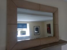A contemporary wall or overmantle mirror having a rectangular plate in a wide cushioned faux suede