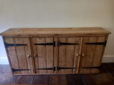 A C.1900 pine sideboard having a rectangular plank top over four panelled cabinet doors with iron
