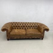 A Victorian style leather Chesterfield two seater sofa with deep buttoned back and scroll arms