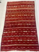 A large Morrocan Kilim carpet with bands of geometric decoration over a burgundy ground. 268x169cm.