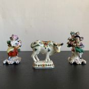 A 20th century Delft polychrome cow with marks along with a pair of Dresden style seated figures