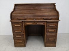 An early 20th century oak roll top desk having a serpentine tambour top enclosing a fitted