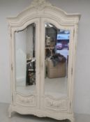 A 19th century painted and distressed French armoire having a scrolling carved cresting and shaped