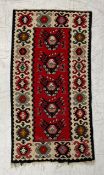 A Turkish Kilim flatweave rug having a single row of five geometric medallions over a box red ground