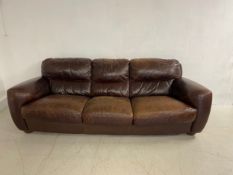 A vintage brown leather three seater sofa with square cushioned back seat and arms raised on