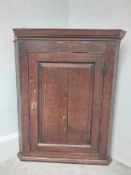 A Georgian oak hanging corner cabinet with panelled door enclosing shelves. H.94 W.75 D.42cm