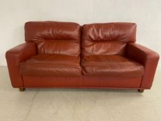 A vintage red leather two seater sofa with square cushioned back seat and arms raised on square