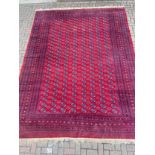 A large bokhara carpet with repeating gul motifs across a burgundy field within multiple stylised