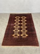 An Eastern rug with repeating lozenge medallions on a sand ground within burgundy multiple