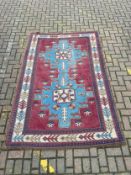 A Kazak carpet with stepped medallions on a burgundy field within stylised multiple borders.