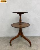 A Georgian mahogany two-tiered dumb waiter with turned stem raised on swept tripod supports on brass