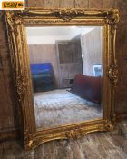 A large 19th century style wall mirror with a rectangular bevelled plate in a heavy scrolling gilt