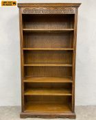 A vintage oak open bookcase with carved frieze over six shelves raised on a shaped plinth base by