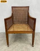 A Regency style mahogany bergere library armchair with square cane back, seat and arms raised on