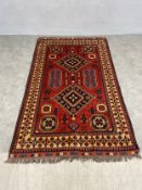 A vintage Afghan Turkomen Kazak carpet with central diamond lozenge medallions over an iron red