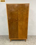 A mid-century teak wardrobe with two figured doors enclosing a hanging section and pigeon holes
