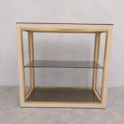 A vintage brass and painted metal etagere with three open smoked glass shelves raised on a square