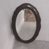 An Edwardian wall mirror with an oval bevelled plate in a scalloped faux rosewood veneered frame.