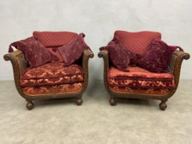 A pair of early 20th century mahogany framed bergere armchairs with ribbon and laurel leaf carving