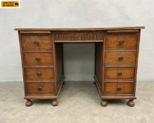 An early 20th century oak kneehole desk with two slides and secret carved frieze drawer over eight