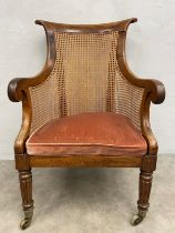 A George IV rosewood framed bergere library armchair with caned back and sides on tapering reeded