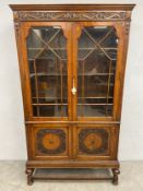 A Jacobean style oak bookcase with astragal glazed doors above carved panel doors on stretchered