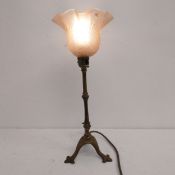 A C.1900 brass table lamp with scalloped pink glass shade raised on tripod supports. H.39cm