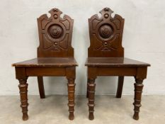 A pair of 19th century oak hall chairs with carved armorial style backs and panel seats on turned
