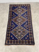 A hand knotted Caucasian Kazak rug with three stepped diamond lozenge medallions over a midnight