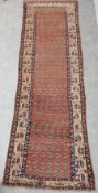 A Kazak runner with repeating motifs on a rust ground within stylised foliate multiple borders. L.