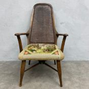 An early 20th century beech framed armchair with shaped rattan back and needlework upholstered