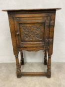 A mid century Jacobean style oak side cabinet with carved panel door on turned stretchered supports.