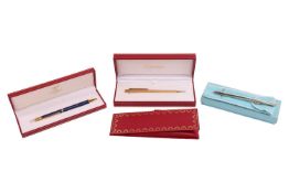 Three pens; comprising a Must de Cartier gilt and blue enamel ballpoint pen, a Must de Cartier gilt 