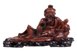 A Chinese cherrywood hand carved figure of a recumbent sage and child, early 20th century, holding a