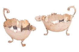 A graduated matched pair of silver sauce boats, of panelled form with applied scrolling borders and 