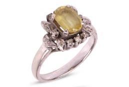 A yellow sapphire and diamond cluster ring, the oval cut sapphire in four claw mount, within a styli