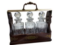 A  Victorian style mahogany three-bottle tantalus, the fall-front base applied with brass cut-card