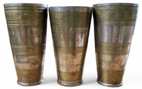 Three Asian silvered metal and brass  tapering cylindrical marriage cups, pin engraved with bands,