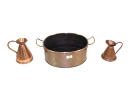 A copper twin handle oval shaped cooking pot and two small copper jugs