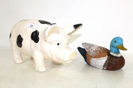 A small painted wooden decoy duck and a ceramic black and white pig