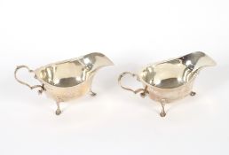 A pair of silver cream jugs having serrated borders, scroll handles and pad feet, Birmingham 1915,