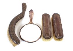 A silver backed hand mirror, a pair of silver backed brushes and a white metal foliate embossed